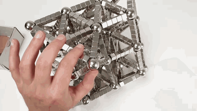 a person is holding a cube made of metal balls and blocks