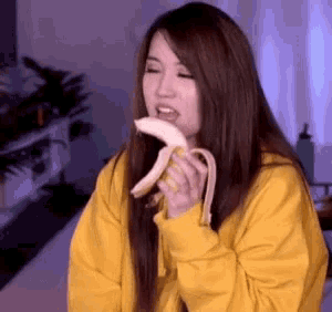 a woman wearing a yellow hoodie is eating a banana .