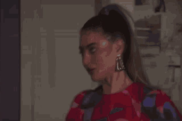 a woman with long hair in a ponytail is wearing earrings and a red dress .