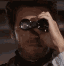 a close up of a man looking through binoculars with his eyes closed