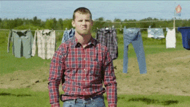 a man in a plaid shirt is standing in front of clothes hanging on a clothes line