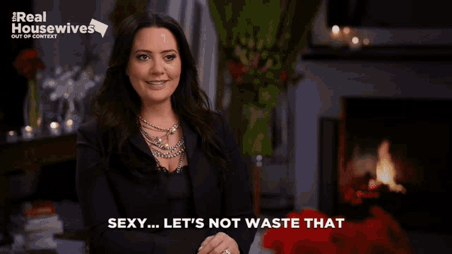 a woman says sexy let 's not waste that while standing in front of a fireplace