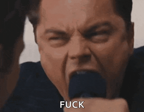 a man in a suit and tie is screaming with his mouth open and says fuck .