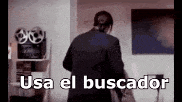 a man in a suit is standing in a living room with the words usa el buscador written on the screen .