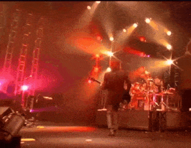 a man is walking on a stage with a drum set in the background .