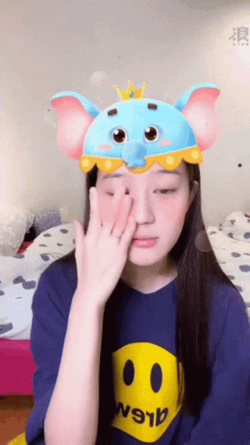a girl wearing a blue shirt with a yellow smiley face and a blue elephant hat