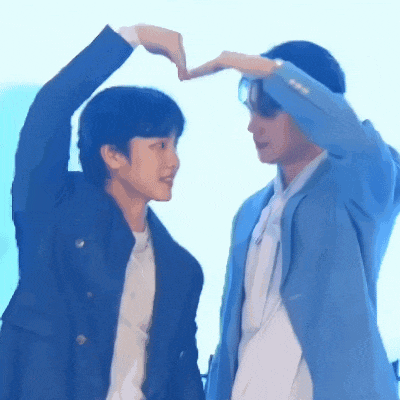 two men are making a heart shape with their hands while standing next to each other .