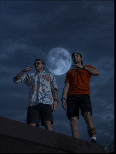 two men standing in front of a full moon in the night sky