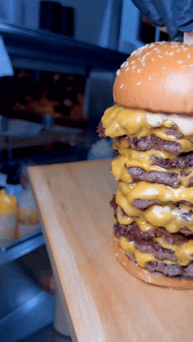 a hamburger with three layers of cheese is sitting on a cutting board