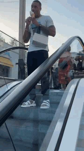 a man is eating an ice cream cone while standing on an escalator