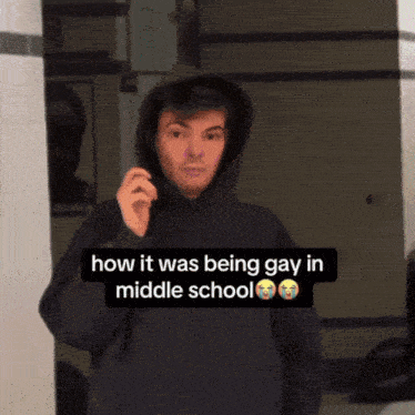 a young man in a black hoodie stands in front of a mirror with a caption that says how it was being gay in middle school