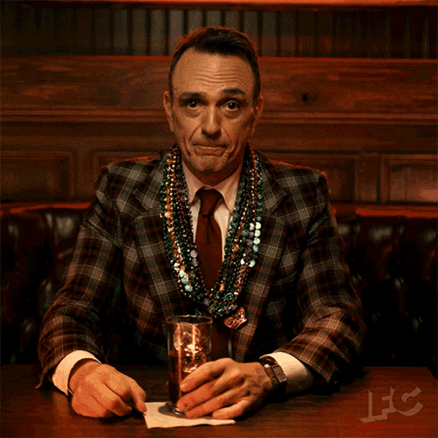 a man in a plaid suit is giving the middle finger while holding a glass of whiskey