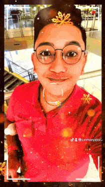 a man wearing glasses and a red shirt is taking a selfie with a snowflake on his head