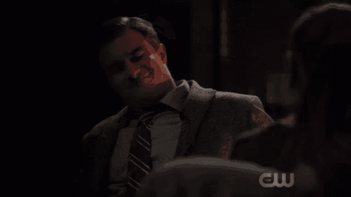 a man in a suit and tie is reading a book with a cw logo on the bottom right