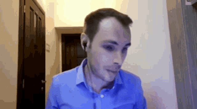 a man in a blue shirt is wearing ear buds and looking at the camera .