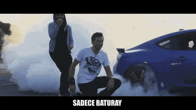 a man and a woman are dancing in front of a car with smoke coming out of the tires
