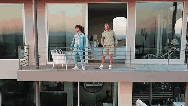 two men standing on a balcony in front of a window