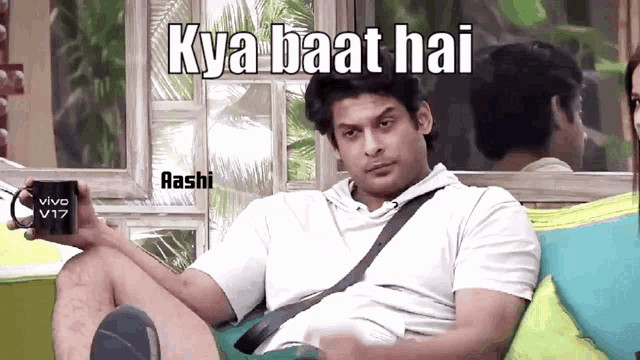 a man is sitting on a couch holding a mug that says " kya baat hai " on it