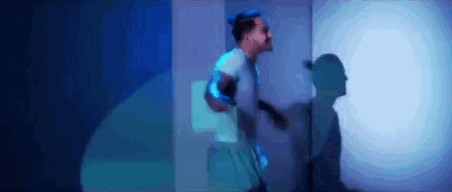a man is running in a dark room with a blue light projected on the wall behind him .