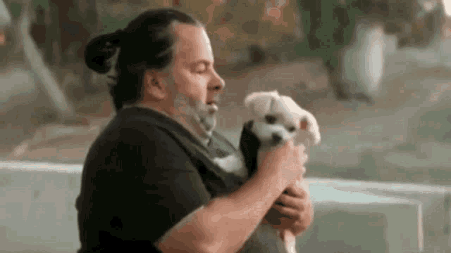a man with a beard is holding a small white dog .