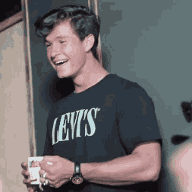 a young man wearing a black levis t-shirt is smiling