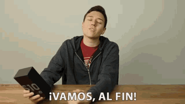 a man sitting at a table holding a box that says ' vamos al fin ' on it