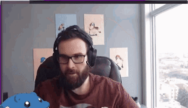 a man with a beard wearing headphones and glasses is sitting in front of a window