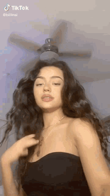 a woman with long curly hair is standing in front of a ceiling fan .