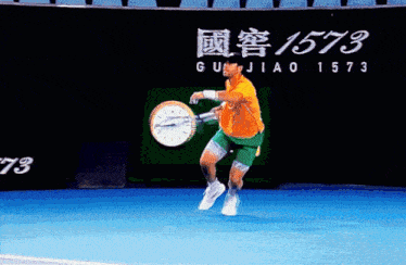 a man is holding a tennis racquet in front of a sign that says guijiao 1573