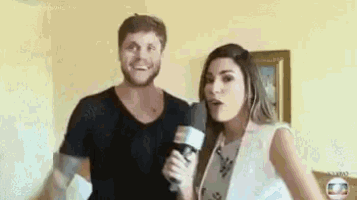 a man and a woman are standing next to each other in a living room . the woman is holding a microphone .