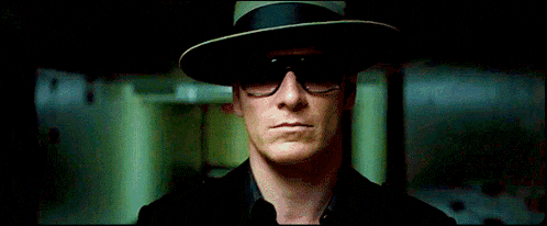 a man in a black hat and sunglasses is standing in a hallway .