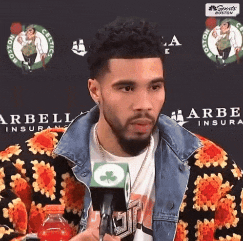 a man talking into a microphone in front of boston celtics logos