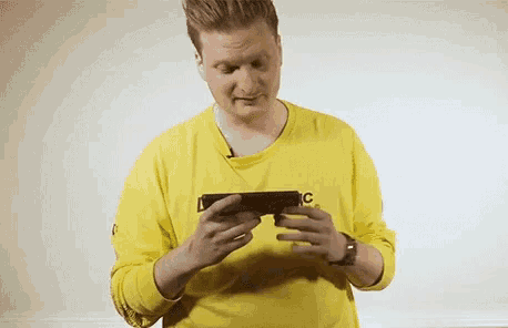 a man in a yellow shirt is holding a cell phone and the word true is above his head