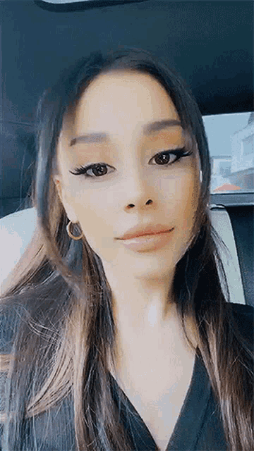 ariana grande is sitting in the back seat of a car wearing a black shirt and earrings .