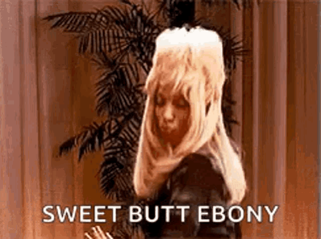 a woman in a wig is standing in front of a palm tree and saying sweet butt ebony .