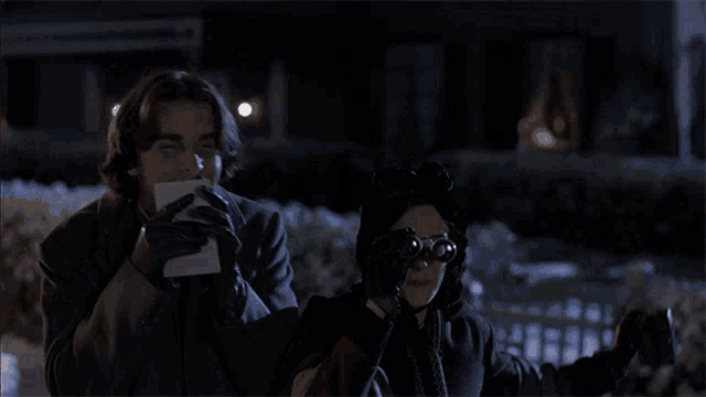 a man holding a piece of paper next to a woman holding binoculars