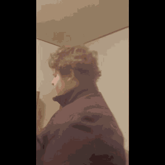 a man with curly hair wearing a purple jacket is standing in a bathroom .