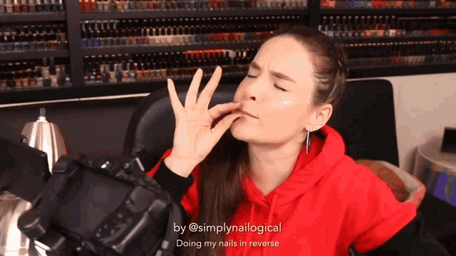 a woman wearing a red hoodie is doing her nails in reverse by @simplynaillogical