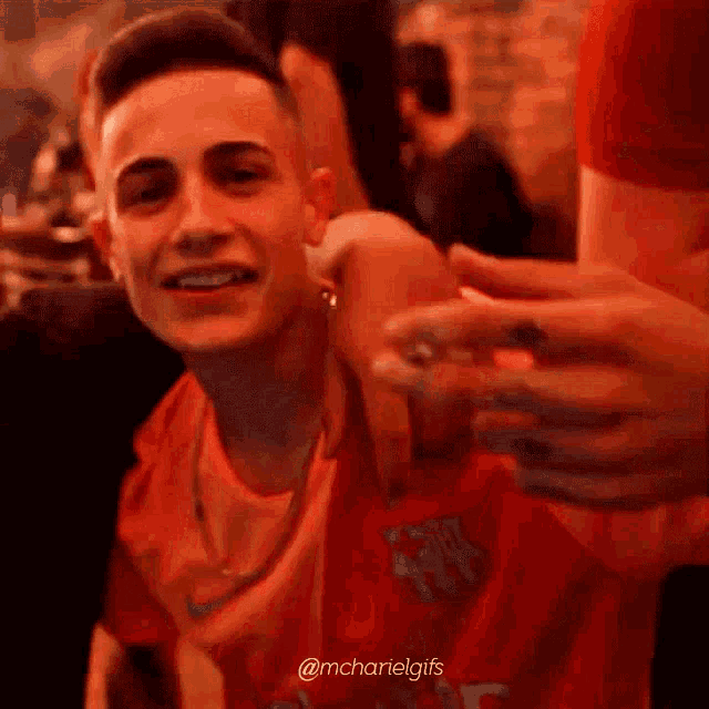 a young man in a red shirt is smiling while sitting in a crowd of people .