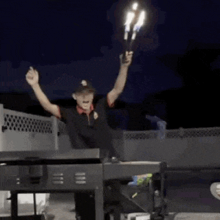 a man is holding two candles in his hands while standing in front of a grill at night .