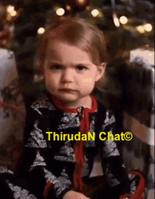 a little girl is sitting in front of a christmas tree and making a face .