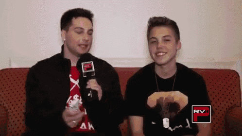 two young men are sitting on a couch and one of them is wearing a shirt that says " rv "