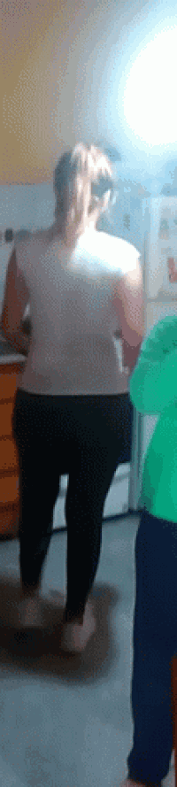 a woman in a pink shirt and black pants stands in a kitchen