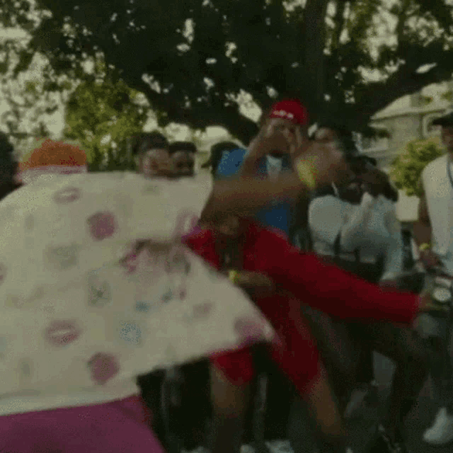 a group of people are dancing in front of a tree in a park .