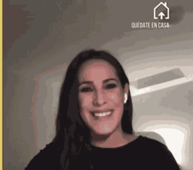 a woman wearing ear buds is smiling in front of a screen that says quedate en casa .