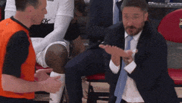 a man in a suit and tie applauds while sitting in a stadium
