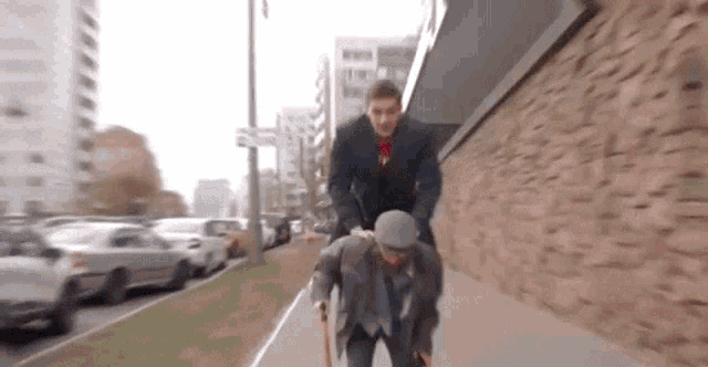 a man is pushing another man with a cane down a sidewalk .