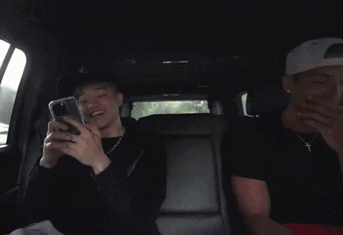 two men are sitting in the back seat of a car and one has a cross on his necklace