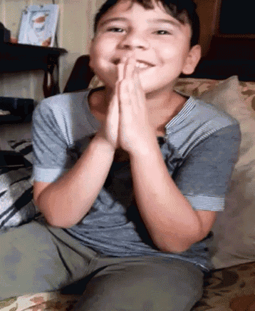 a young boy is sitting on a couch with his hands folded in front of his face