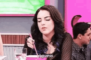 a woman is sitting at a table with a drink in her hand and a straw .
